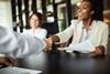 Image of a businesswoman smiling and shaking someone's hand across a table