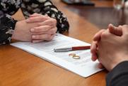 A divorcing couple sit across a table, their wedding rings sat on the divorce papers