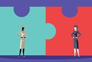 Two giant, connected jigsaw pieces with two women standing in front looking at each other