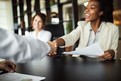 Image of a businesswoman smiling and shaking someone's hand across a table