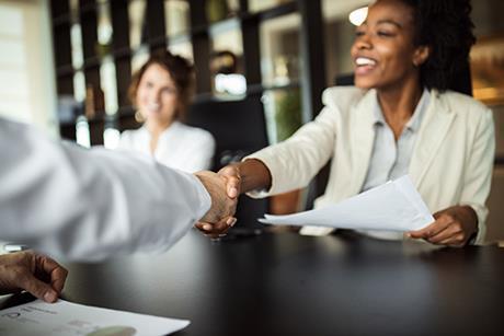 Image of a businesswoman smiling and shaking someone's hand across a table