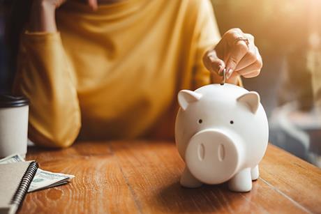 Image of a woman's hand putting a coin into a piggy bank